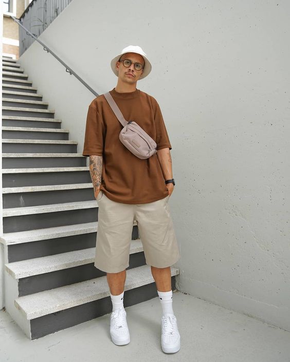 a neutral summer look with a brown oversized t shirt, grey Bermuda shorts, white sneakers and socks, a bucket hat and a waist bag