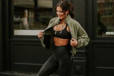 a sport chic look with a black bra, black leggings, white sneakers, an olive green sweatshirt with a zip