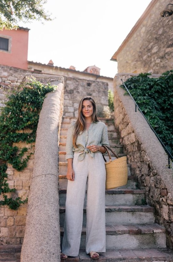 a summer outfit with a grey linen shirt, neutral linen pants, tan slides and a straw bag is a lovely idea for a hot day or vacation