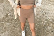 a taupe co-ord workout look with a bra top and biker shorts, white trainers and socks, a grey hoodie on top