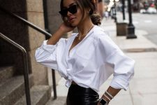 a white knotted shirt, a black leather midi skirt with a slit, a chic black tote and statement jewelry