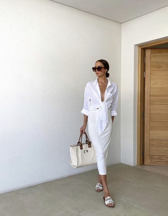 an all-white outfit wiht a white knotted shirt, a creamy midi pencil skirt, white printed slippers and a tote