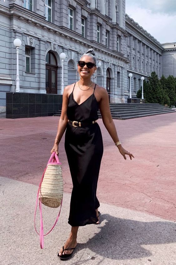 an easy and chic summer look with a black slip midi dress with a belt, black slippers, a straw bag with hot pink details