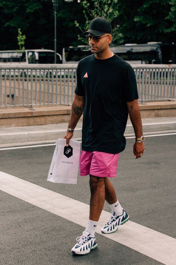an easy sport look with a touch of color, a black oversized t-shirt, hot pink shorts, green and white trainers and white socks