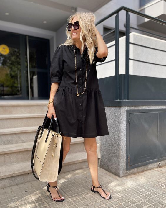 a black over the knee shirtdress with short sleeves, a long necklace, black sandals and a neutral tote for summer