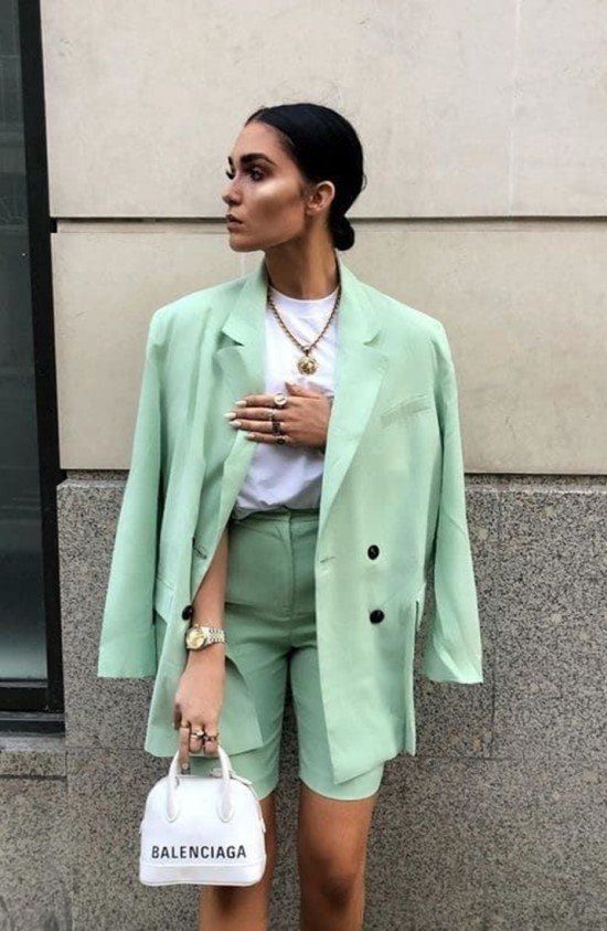 a light green suit with a blazer and Bermuda shorts, a white t-shirt, a statement necklace and a small white bag