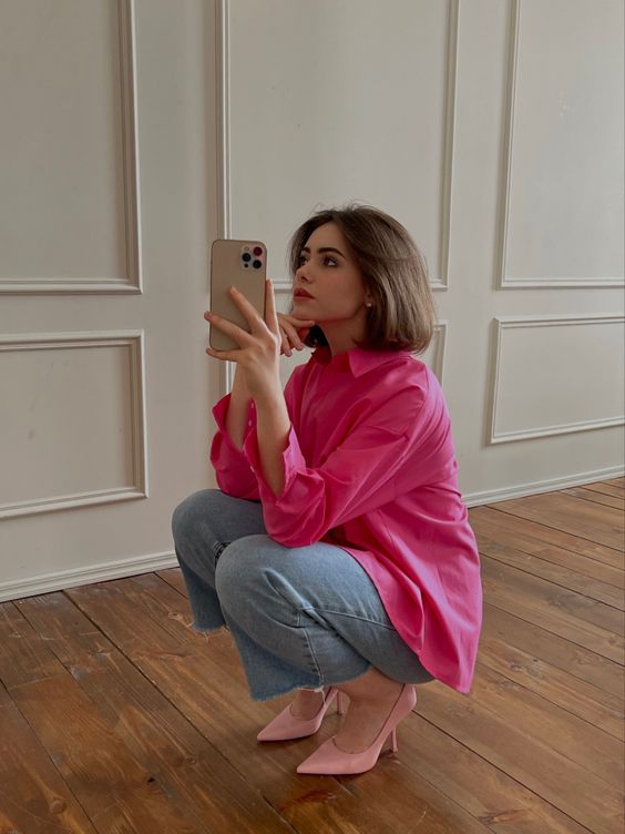 a hot pink shirt, blue jeans and light pink shoes compose a super bold and catchy work look
