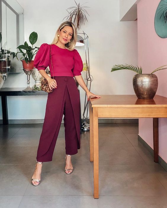 a refined monochromatic work look with a fuchsia top with puff sleeves and burgundy pants, silver shoes and a printed bag