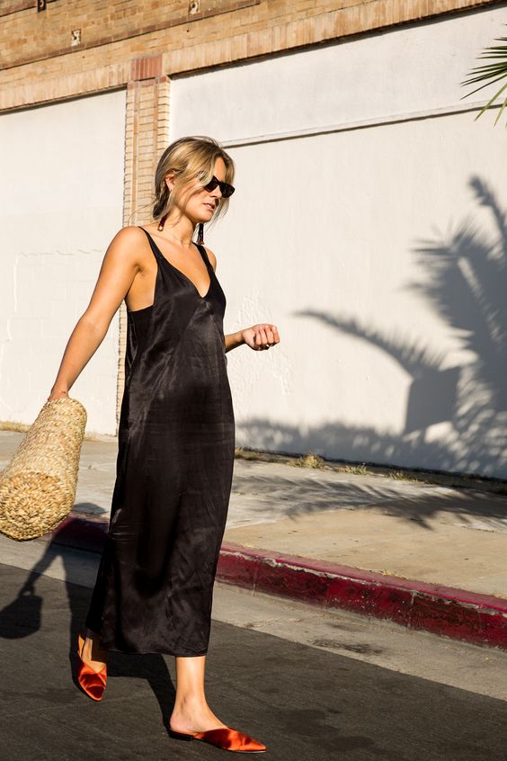 a black silk slip midi dress with a deep neckline, fiery red slippers and a woven bag for hot weather