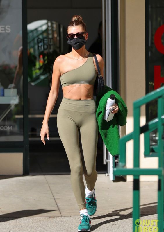 Hailey Bieber wearing a green sport set with a one shoulder bra top, leggigns, emerald trainers and a black bag