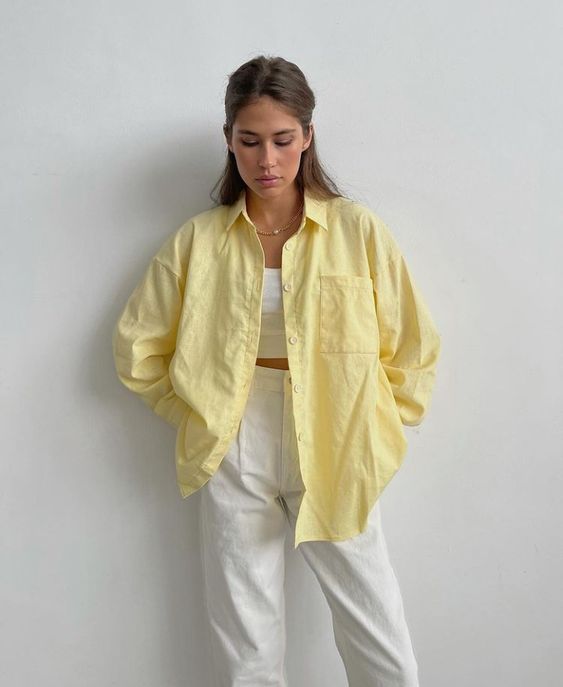 a white crop top, white linen trousers and a bold yellow oversized shirt on top that brings color and interest to the look