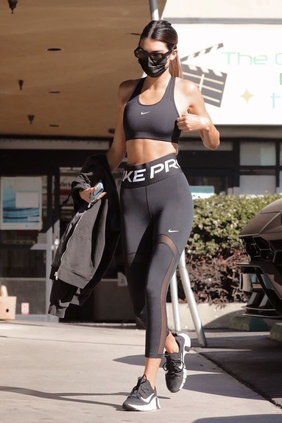 Kendall Jenner workout look with a black bra top, high waisted leggings, black trainers and a black cover up
