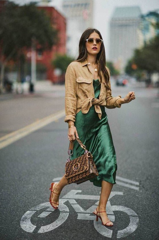 a creative summer work look with a green slip midi dress, a linen tan shirt over it, red heels and a printed bag