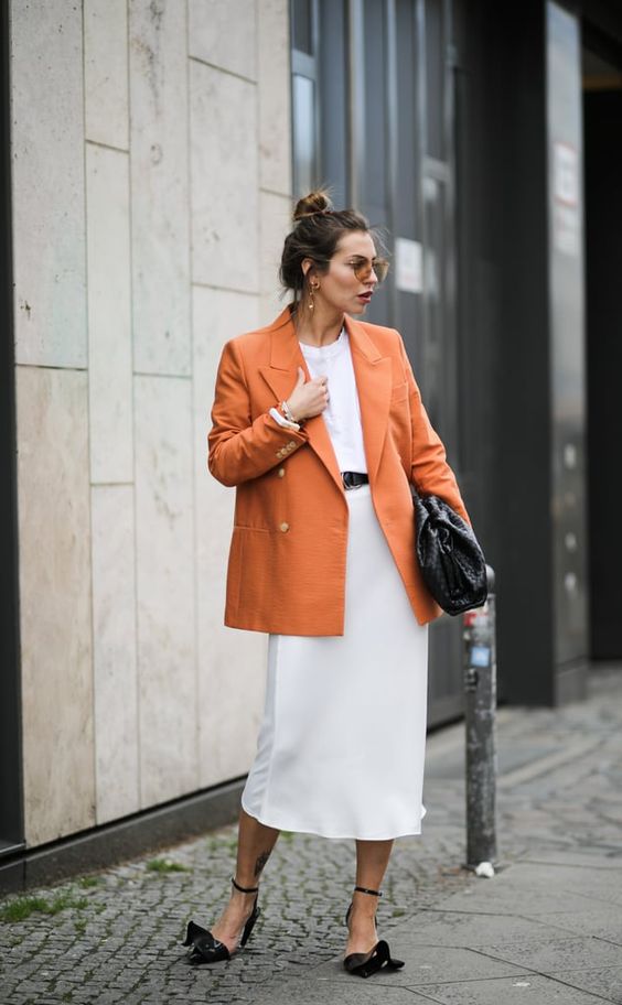 a white t-shirt, a neutral midi slip skirt, an orange oversized blazer, a black bag and black heels