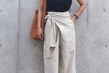 With light gray linen belted wrap palazzo pants, brown tote bag, suede high heeled sandals, golden earrings and sunglasses