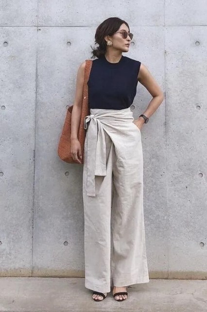 With light gray linen belted wrap palazzo pants, brown tote bag, suede high heeled sandals, golden earrings and sunglasses