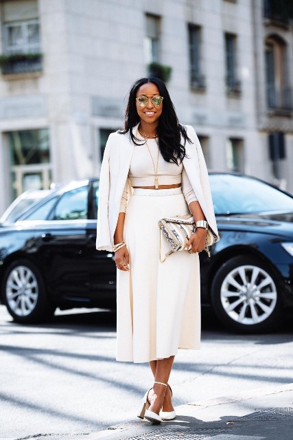 With mirrored sunglasses, white high-waisted midi skirt, white ankle strap shoes and printed chain strap bag