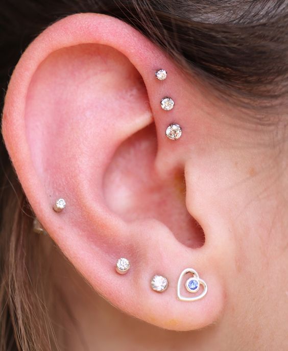 a bold and cool ear look with a triple forward helix piercing done with matching studs, a triple lobe and a helix piercing