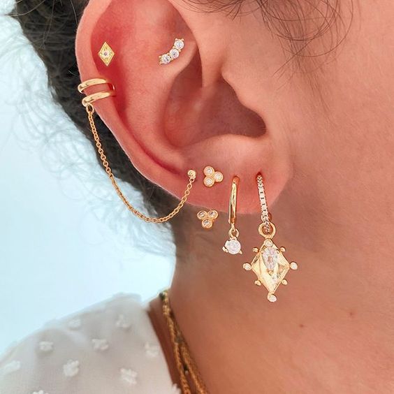 a bold ear with a faux rook, double helix, multiple lobe piercings done with gold hoops and studs is wow
