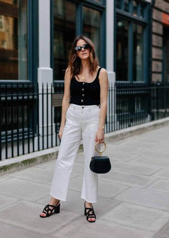 a chic look with a black button up top, white jeans, black block heels and a black bag with a ring handle