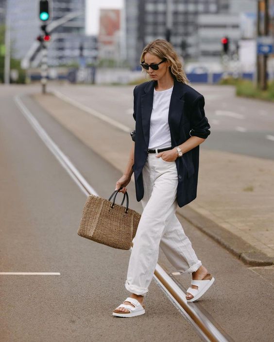 a cool summer work look with a white t shirt, white jeans, an oversized black blazer and a black belt, white birkenstocks and a woven bag