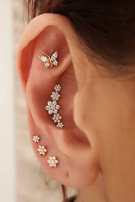 a girlish ear stack with multiple lobe, a conch and a faux rook piercing all done with floral and butterfly studs