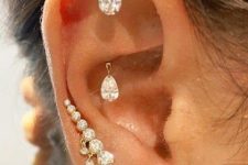a gkan abd shiny ear with a hidden helix and rook piercings done with large crystals and two lobe piercings with studs