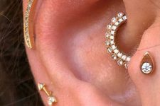 a glam ear with a faux rook, flat, helix, tragus, daith and a triple lobe piercing done with gold studs and hoops
