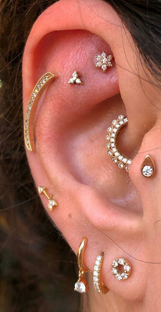 a glam ear with a faux rook, flat, helix, tragus, daith and a triple lobe piercing done with gold studs and hoops