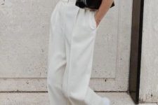 a minimalist summer outfit with a black shirt, white wide leg pants, white sneakers and a small black bag