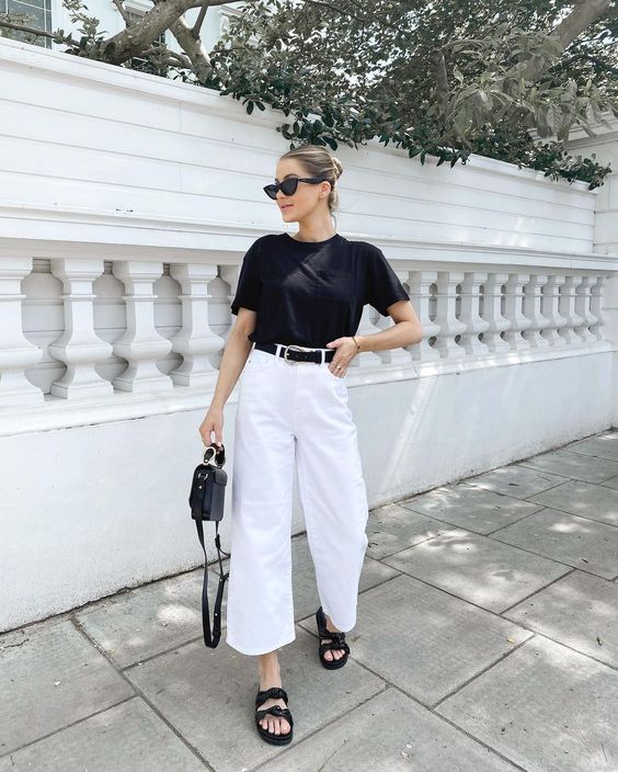 a minimalist work outfit with a black t shirt, white wideleg jeans, a black belt and sandals plus a black bag