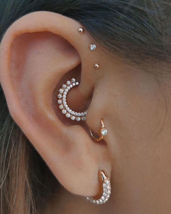 a refined ear set with a triple forward helix piercing, a daith, tragus and lobe one, all done with matching studs and hoops