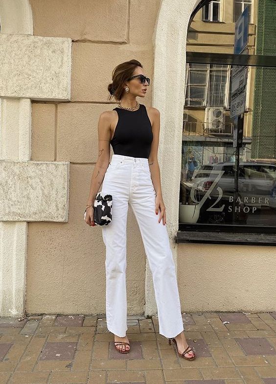 a refined work outfit with a black halter neckline bodysuit, white high waisted jeans, brown strappy shoes and a printedbag