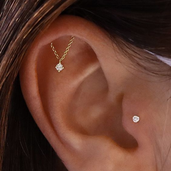 a subtle ear set with a hidden helix and a tragus piercing done with a stud and a gold chain with a rhinestone