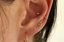 a subtle ear stack with mutiple lobe, conch, forward helix and faux rook piercing done with gold hoops, studs and even chains