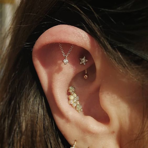 a super glam ear look with a conch, rook and hidden helix piercing with various studs and a chain with a rhinestone