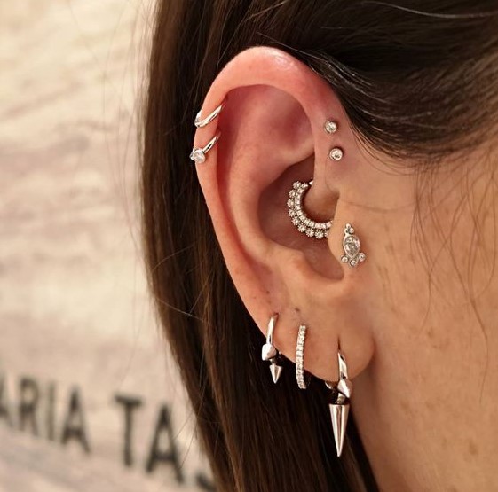 a triple lobe piercing done with bold hoop earrings, a double helix, a double forward helix piercing, a daith and a tragus one