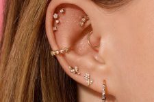 a very delicate ear stack with a faux rook, daith, triple lobe, conch and several helix piercings done with studs and hoops