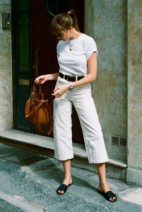a white tee, white cropped jeans, a black belt, black slides and an amber-colored bag for a simple work look