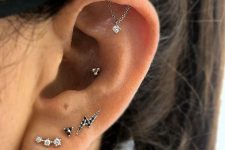 an edgy ear set with a triple lobe, conch and hidden helix piercing done with black and white studs and a chain with a rhinestone