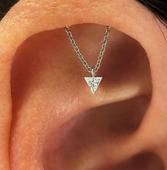 an invisible helix piercing with a chain and a triangle rhinestone, which is a unique jewelry piece that will add interest to your look