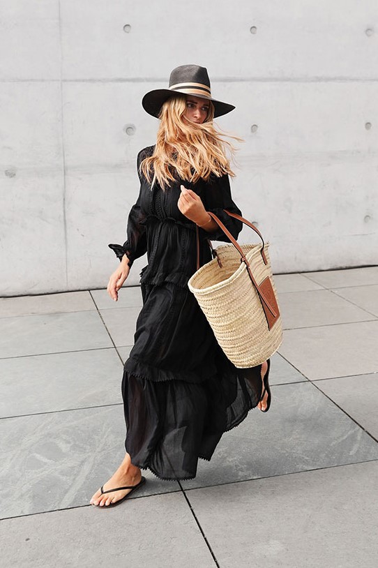 a black maxi dress with long sleeves, black flipflop sandals, a straw tote bag and a black hat for a bold and contrasting look