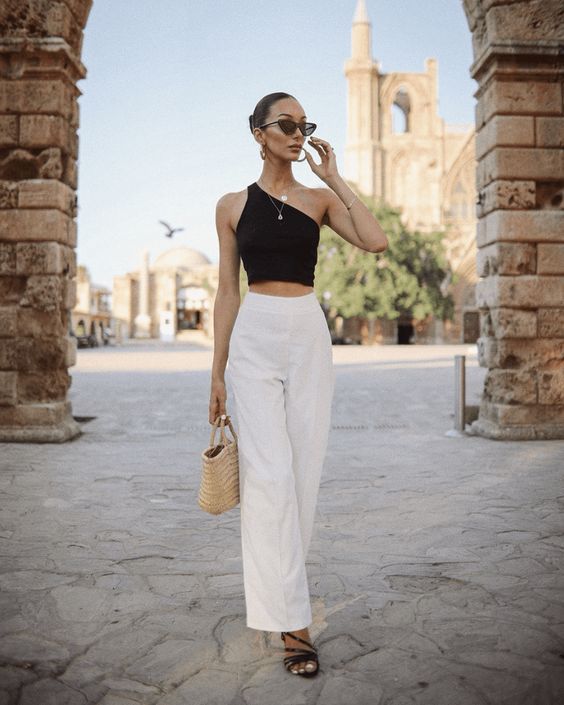 a black one shoulder crop top, white high waisted pants, black strappy heels and a woven bag for an elegant minimal look