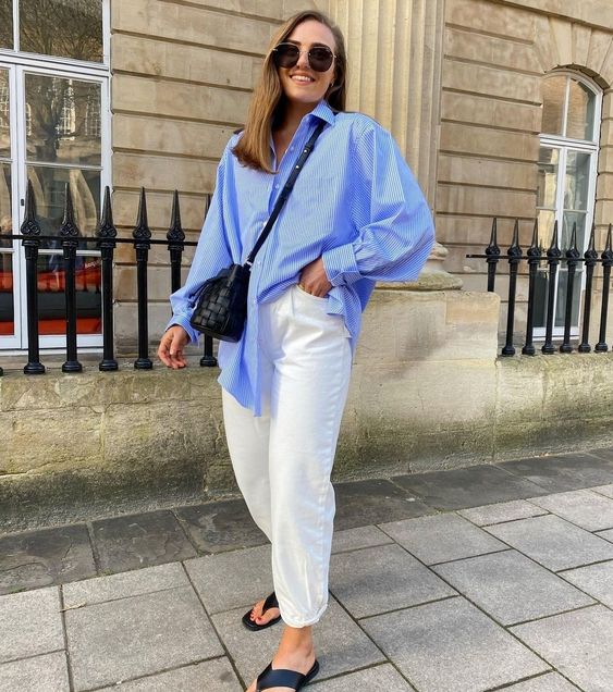 a blue oversized thin striped shirt, white jeans, black flipflops and a black woven bag