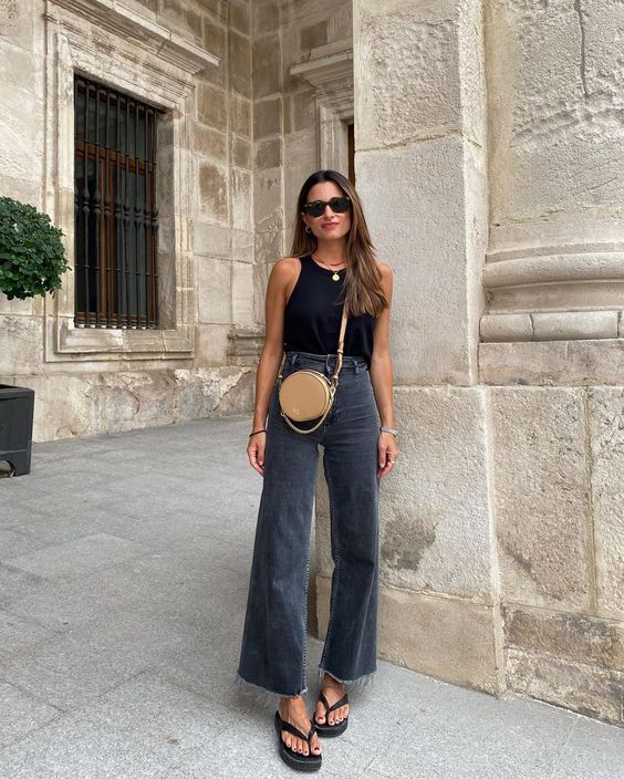 a minimalist every day look with a black halter neckline top, black flare high waisted jeans, black slippers and a round bag in beige