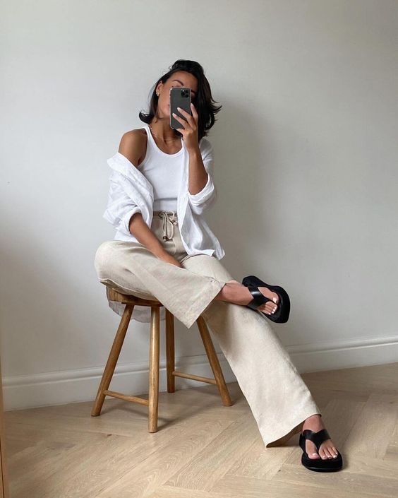 a minimalist neutral summer outfit with a white tnak top, a white shirt, tan flare jeans and black flipflops