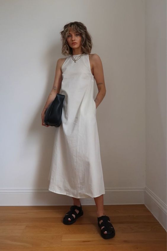a minimalsit look with a white A-line midi dress with a halter neck, black sandals and a black bag plus layered necklaces