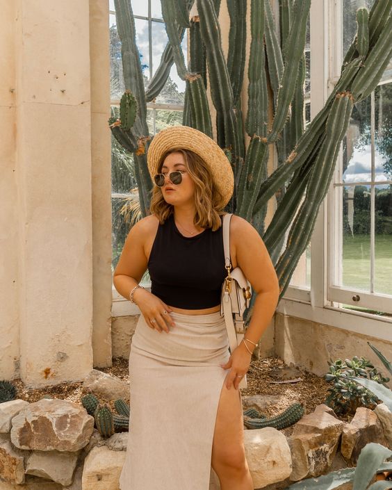 a black crop top, a neutral midi skirt with a thigh high slit, a straw hat and a small neutral bag for a sexy vacation look