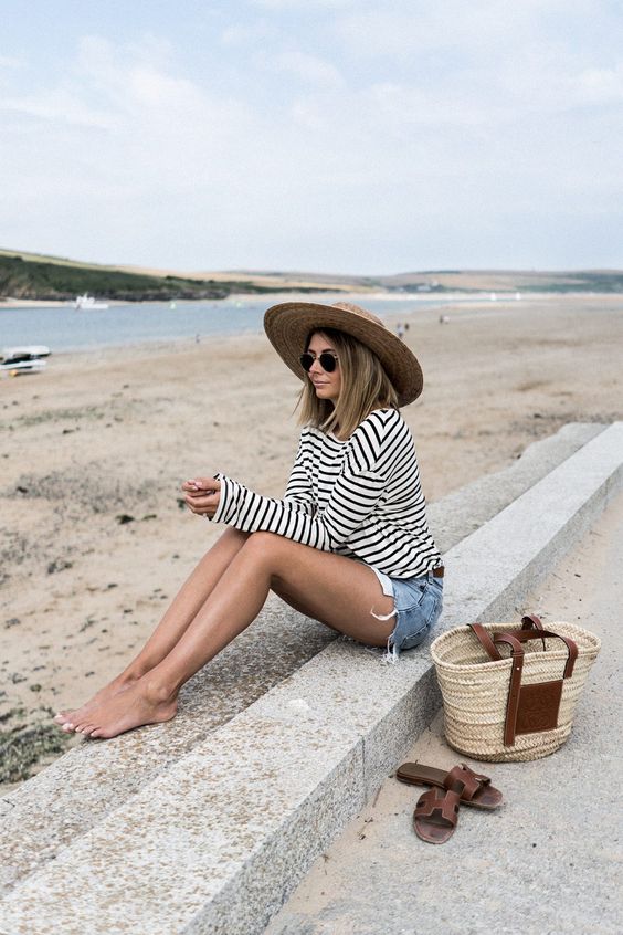 a Breton stripe long sleeve t-shirt, blue denim shorts, a straw tote and a wide brim hat for a warm day