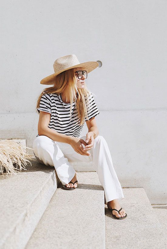 a black and white stripe t-shirt, white pants, minimalist flipflops, a wide brim straw hat and glasses